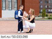 A first-grader boy gives autumn flowers to a teacher on 1st September in the school yard. Tradition to give flowers to the teacher on the first day of school. Knowledge Day. Teacher's Day. Стоковое фото, фотограф Ирина Михайличенко / Фотобанк Лори