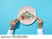 Fish from colorful pills and tablets on a white plate with girl’s hands with watch on a blue background with shadows, copy space. Top view. Colorful food supplement pills.. Vitamin pills and tablets in the shape o a fish in a plate and woman’s hand with watch on a blue background. Flat lay. Стоковое фото, агентство Ingram Publishing / Фотобанк Лори
