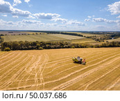 Aerial view from drone to harvest of wheat crops by agricultural combines in a sunny summer day on a background of blue sky.. Countryside landscape aerial view from drone to agricultural field with combine on a blue sky background. Стоковое фото, агентство Ingram Publishing / Фотобанк Лори