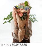 Woman’s hands with tattoo hold floral bouquet of living coral color roses and green leaf on a white background. Place for text. Concept of Mother’s Day.. Wonderful bouquet from coral color roses and eryngium in girl’s hands on a light background with green leaf. Copy space. Greeting post card. Стоковое фото, агентство Ingram Publishing / Фотобанк Лори