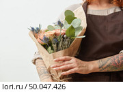 Woman’s hands with tattoo are holding beautiful colored living coral rores bouquet. Greeting holiday card for Mother’s or Woman’s Day. Place for text.. Fresh flowers living coral roses and eryngium as a congratulate bouquet in girl’s hand with tattoo, copy space. Post card for Mother’s Day. Стоковое фото, агентство Ingram Publishing / Фотобанк Лори