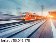 Modern high speed red passenger commuter train in motion at the railway platform at sunset. Railway station. Railroad with motion blur effect. Industrial landscape with train. Vintage toning. Стоковое фото, агентство Ingram Publishing / Фотобанк Лори