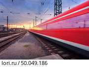 High speed red passenger train on railroad track in motion at sunset. Blurred commuter train. Railway station in Nuremberg, Germany. Industrial landscape. Стоковое фото, агентство Ingram Publishing / Фотобанк Лори