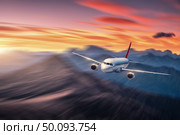 Airplane in motion. Aircraft with motion blur effect is flying over hills and mountains at sunset. Passenger airplane, blurred clouds. Passenger aircraft in motion. Business travel. Commercial.Concept. Стоковое фото, агентство Ingram Publishing / Фотобанк Лори