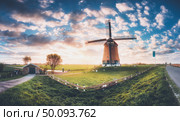 Windmill at sunrise in Netherlands. Amazing view with traditional dutch windmill, green grass, fence and colorful sky with clouds. Rustic landscape with vintage toning. Rural scene in summer. Travel. Стоковое фото, агентство Ingram Publishing / Фотобанк Лори