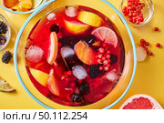 Drink with different berries and fruits with ice cubes in a glass jug presented on a yellow background. Top view. Top view on glass jug with homemade fruit berry drink with ice cubes on yellow background. Стоковое фото, агентство Ingram Publishing / Фотобанк Лори