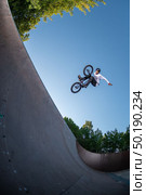 Biker jump high from quarter pipe ramp performing hands off the handlebars trick. Стоковое фото, агентство Ingram Publishing / Фотобанк Лори