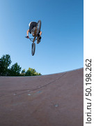 Biker jump high from jump box ramp performing 360 trick. Стоковое фото, агентство Ingram Publishing / Фотобанк Лори
