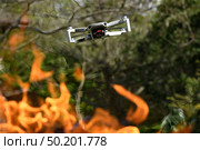 Flying drone Quadcopter with camera pointed at viewer outdoor in a fire in the foreground spurts of flame forest background. Стоковое фото, фотограф Camptoloma / Фотобанк Лори