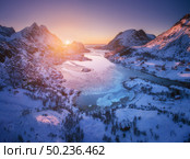Aerial view of snowy mountains, sea, purple sky at sunset in Lofoten islands, Norway. Winter colorful landscape with snow covered rocks, frosty seacoast, road and village. Top view of Norwegian Fjords. Стоковое фото, агентство Ingram Publishing / Фотобанк Лори