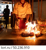 Cooking of beef teppanyaki recipe japanese grilled beef tomahawk steak on cooking pan using scraper with flame in background. Стоковое фото, агентство Ingram Publishing / Фотобанк Лори