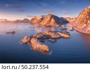 Aerial view of rocks in the sea, snowy mountains, blue sky with clouds at sunset. Travel in Lofoten Islands, Norway. Winter landscape with small islands in water, cliffs and waves. View from above. Стоковое фото, агентство Ingram Publishing / Фотобанк Лори