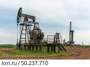 Oil production at the field using two rocking machines. In the background is a drilling rig and equipment for drilling wells. Summer. Beautiful sky and nature. Стоковое фото, фотограф Владимир Ендовицкий / Фотобанк Лори