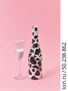Holiday glass of white powder as a sugar and painted bottle with black spots on a light millennial pink background, copy space. Congratulation card.. Creative painted wine bottle with black spots and glass of white powder. Стоковое фото, агентство Ingram Publishing / Фотобанк Лори