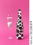 Decorative white painted wine bottle with black spots and glass with falling white powder on a hot pink background, place for text. Congratulation card.. White powder falls in a glass and painted black spots wine bottle. Стоковое фото, агентство Ingram Publishing / Фотобанк Лори