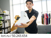 Social media influencer reviewing fashion shoe. Smiling young man vlogging about men’s sports shoe and filming himself at home on a video camera. Стоковое фото, агентство Ingram Publishing / Фотобанк Лори