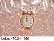 Golden alarm clock with time is midnight on a shiny cooper abstract background with string of lights, copy space. Greeting card.. Christmas exact time on an old-fashioned cooper alarmclock. Стоковое фото, агентство Ingram Publishing / Фотобанк Лори