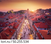 Aerial view of beautiful old city at sunset. Top view of houses with red roofs, city lights, historical centre, architecture, walking people in illuminated streets at night in Dubrovnik, Croatia. Стоковое фото, агентство Ingram Publishing / Фотобанк Лори