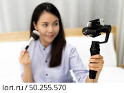 Young beautiful Asian woman beauty vlogger or blogger recording live how to make up tutorial to share on social media using Gimbal Stabilizer on mobile phone. Using for vlog social media influencer concept. Focus on Stabilizer. Стоковое фото, агентство Ingram Publishing / Фотобанк Лори