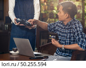 Asian customer using credit card with EMV chip technology to pay a waitress for coffee purchase at table in cafe. Стоковое фото, агентство Ingram Publishing / Фотобанк Лори