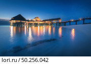 Beautiful wooden restaurant on the water in summer night. Landscape with hotel on the sea, illumination, jetty, sandy beach, blue sky and lights reflected in blurred water at dusk in Zanzibar, Africa. Стоковое фото, агентство Ingram Publishing / Фотобанк Лори