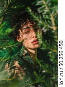 A curious young womans face emerges amongst vibrant green leaves, sunlight creating a dappled effect on her skin. Стоковое AI-изображение, AI-художник Данила Большаков / Фотобанк Лори