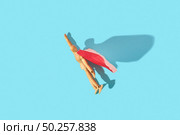 Wooden mannequin miniature doll in a red cape with raised hand flies up as a superman or superhero on a light blue background, copy space. Business success and leadeship concept.. Movable human miniature model in red cape as a superman flies up. Стоковое фото, агентство Ingram Publishing / Фотобанк Лори