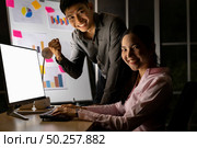 Young adult asian businessman and businesswoman work with analysis graph on white board late at night in their office with desktop computer. Using as hard working and working late concept. Стоковое фото, агентство Ingram Publishing / Фотобанк Лори