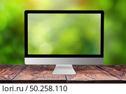 Green blurred computer monitor on a wooden table against the same natural background with bokeh, copy space. Working on nature, outside office concept.. Monitor with blurred screen and background. Стоковое фото, агентство Ingram Publishing / Фотобанк Лори