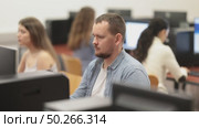 Man student of computer courses looks at monitor screen, types on keyboard and does work. Стоковое видео, видеограф Яков Филимонов / Фотобанк Лори