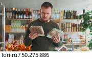 Young European man chooses seasonal mushrooms in the food section next to the counter. Supermarket visitor holds packs of champignons and oyster mushrooms in his hands. Стоковое видео, видеограф Яков Филимонов / Фотобанк Лори