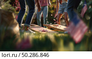 Outdoor gathering features people enjoying cornhole games on a sunny day with flags in the background. Стоковое AI-изображение, AI-художник Сергей Толмачёв / Фотобанк Лори