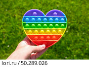 Popit - Colorful antistress sensory toy. Silicone toy - pop it in teen hand on green nature background. Rainbow color, concave and convex bubbles. Trend of summer 2021. Entertainment for children. Стоковое фото, фотограф Марина Демидюк / Фотобанк Лори