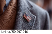 Man wearing a grey suit with an American flag lapel pin in a formal setting during the evening. Стоковое AI-изображение, AI-художник Сергей Толмачёв / Фотобанк Лори