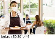 Portrait attractive asian waitress wear face mask and face shield holding food tray to serving meal to customer with custome in background. New normal restaurant concept. Стоковое фото, агентство Ingram Publishing / Фотобанк Лори