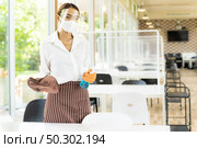 Portrait attractive asian waitress wear face mask and face shield hold alcohol and wet wipe for cleaning table before welcome customer. New normal hygiene restaurant concept. Стоковое фото, агентство Ingram Publishing / Фотобанк Лори