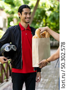 Asian delivery man pick up bakery grocery bag from bakery shop to deliver to customer who make online order. Online food delivery service concept in new normal after coronavirus pandemic. Стоковое фото, агентство Ingram Publishing / Фотобанк Лори