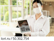 Asian waitress with face mask and face shield hold digital tablet with QR code for customer to scan for online contactless menu. Online contactless and technology concept for new normal restaurant. Стоковое фото, агентство Ingram Publishing / Фотобанк Лори