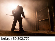 Silhouette of firefighter use metal hook to push away metal door for escape from burning building. Firefighter training  safety rescue from accident and public service concept. Стоковое фото, агентство Ingram Publishing / Фотобанк Лори