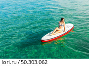 A beautiful woman sitting over a paddle surfboard and relaxing on a beautiful sunny day. Стоковое фото, агентство Ingram Publishing / Фотобанк Лори
