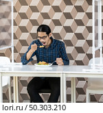 Portrait of asian young adult man eat fried rice food at new normal social distance restaurant with table shiled partition. Restaurant new normal lifestyle and food concept. Стоковое фото, агентство Ingram Publishing / Фотобанк Лори