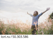Young beautiful woman standing stretch her arms in the air on the grass field. Woman enjoy with nature during sunset. Стоковое фото, агентство Ingram Publishing / Фотобанк Лори