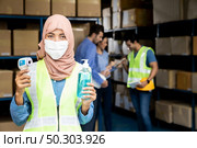 Asian Islam Muslim female warehouse worker with face mask hold hand sanitizer and infrared thermometer. For New normal hygiene life in business warehouse inventory and logistic concept. Стоковое фото, агентство Ingram Publishing / Фотобанк Лори