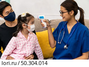 Asian female doctor use infrared thermometer to take temperature to little girl child sit with her dad in living room while doctor visit at home. Home health care delivery and doctor visiting concept. Стоковое фото, агентство Ingram Publishing / Фотобанк Лори