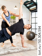 White caucasian man learning yoga at home. Female instructor or trainer coaching and adjust correct side plank pose to student. Workout healthy lifestyle and Yoga health delivery concept. Стоковое фото, агентство Ingram Publishing / Фотобанк Лори