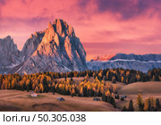 Beautiful mountains with lighted peaks and red sky at sunset. Autumn landscape with small wooden houses, mountain valley, meadows with green grass, fall trees, high rocks. Alpe di Siusi in Italy. Стоковое фото, агентство Ingram Publishing / Фотобанк Лори