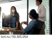 Three asian business person discuss their work in morning after office reopen due to coronavirus COVID-19 pandemic. They wear protective face mask to prevent infection. New normal office life concept. Стоковое фото, агентство Ingram Publishing / Фотобанк Лори