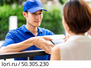 Asian deliver man handling package box to asian woman in front of house and female customer sign electronic signature to portable mobile device. Package shopping delivery and digital sign concept. Стоковое фото, агентство Ingram Publishing / Фотобанк Лори