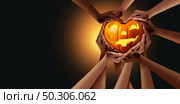 Halloween community group and pumpkin shaped as a heart as a jack o lantern seasonal symbol with a group of diverse people holding a happy seasonal gourd on a black background. Стоковое фото, агентство Ingram Publishing / Фотобанк Лори