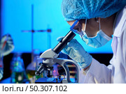 Profile view of concentrated Asian microbiologist examining sample with help of modern microscope while wrapped up in work at dim laboratory. Стоковое фото, агентство Ingram Publishing / Фотобанк Лори